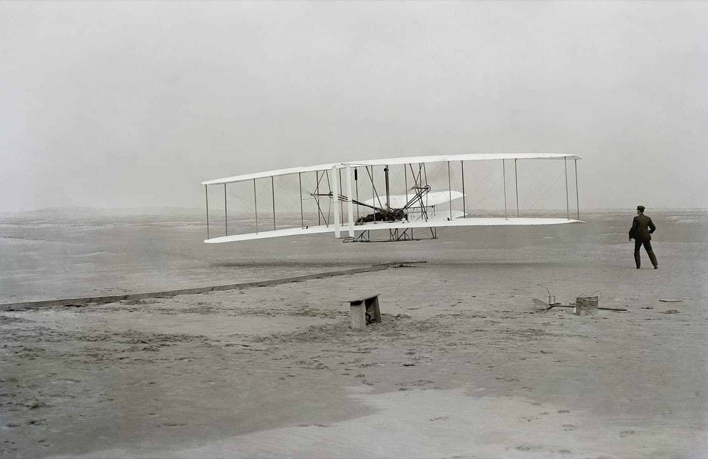 The Wright Flyer a few feet off the sand at Kill Devil Hills, 17 December 1903, with Orville at the controls and Wilbur running alongside